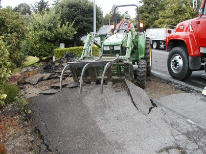 A tractor is working on an asphalt road in front of a house.